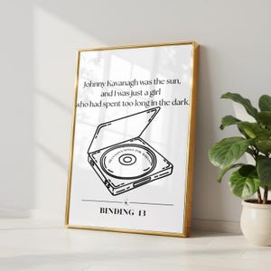 May include: A framed vertical print featuring black line art of an open CD player with a disc inside labeled SHANNONS SONGS FOR JOHNNY. Above the illustration is the text Johnny Kavanagh was the sun, and I was just a girl who had spent too long in the dark. Below is the text BINDING 13.