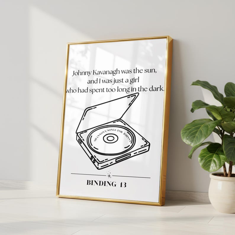 May include: A framed vertical print featuring black line art of an open CD player with a disc inside labeled SHANNONS SONGS FOR JOHNNY. Above the illustration is the text Johnny Kavanagh was the sun, and I was just a girl who had spent too long in the dark. Below is the text BINDING 13.