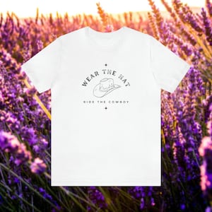 May include: White t-shirt with a black and white graphic of a cowboy hat and the text "Wear the Hat, Ride the Cowboy".