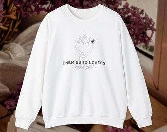 Op de afbeelding: Witte trui met een zwart-witte afbeelding van een hart met een zwaard erdoorheen. De tekst "Enemies to Lovers - Book Club -" staat onder de afbeelding.