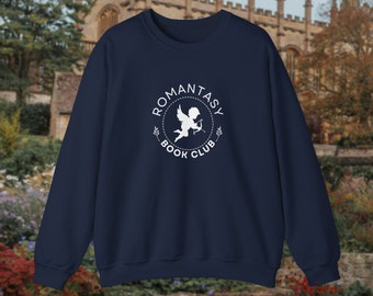 May include: A navy blue sweatshirt with a white circular logo that reads "ROMANTASY BOOK CLUB" and features a cupid. The sweatshirt has a crew neck and is a solid colour.
