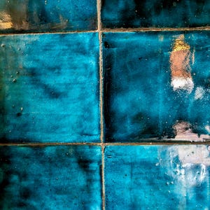 May include: Close-up of six square, glazed ceramic tiles in shades of teal and dark blue. The tiles are arranged in a grid pattern, with visible grout lines. The glossy surface reflects light, creating highlights.