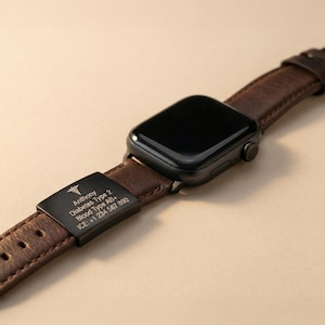 May include: Black smartwatch with a brown leather strap. The strap has a black metal plate with engraved text: "Anthony, Diabetes Type 2, Blood Type AB+, ICE: +1 234 567 890". The watch has a black screen and a red button.