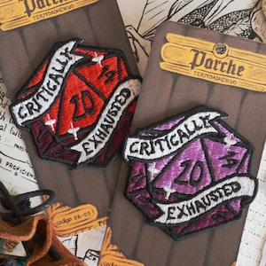 May include: Two embroidered patches featuring a twenty-sided die design. One is red, the other purple, both with the text "CRITICALLY EXHAUSTED" and "20". Each patch is mounted on a brown card with the brand name "Parche".