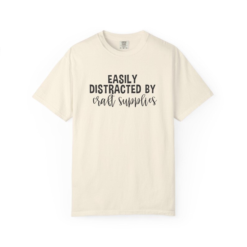 May include: A white ceramic mug with a black handle and the text "But First, Coffee" in a bold, black font. The mug is set against a blurred background, suggesting a cozy setting.