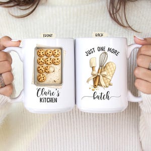 May include: White ceramic mug with the text "Claire's Kitchen" and a tray of chocolate chip cookies. The back of the mug features the text "Just One More Batch" with illustrations of baking tools, including a whisk and oven mitt.
