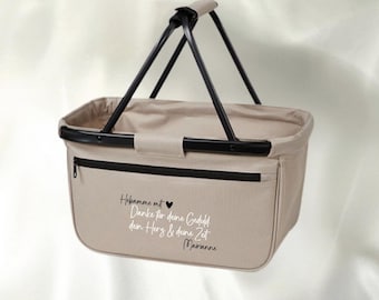 May include: A beige rectangular shopping basket with a black metal frame and handle. The front features a black zippered pocket with the German text: Hebamme mit Herz Danke für deine Geduld dein Herz & deine Zeit Marianne, printed in black and white.