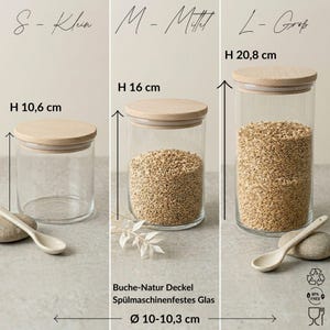May include: Three clear glass storage jars with light wood lids in sizes S, M, and L. Heights are 10.6 cm, 16 cm, and 20.8 cm, with a diameter of 10-10.3 cm. The jars feature natural beech wood lids and dishwasher-safe glass construction.