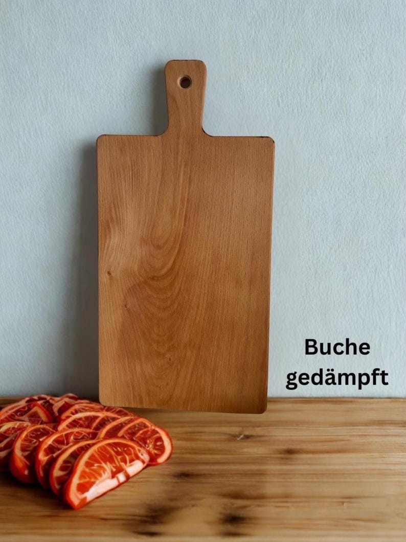 May include: A rectangular wooden cutting board with a handle and a circular hole at the top. The board has a light brown wood grain pattern. To the bottom left, there are several sliced orange citrus fruits. The text Buche ged&auml;mpft is visible.