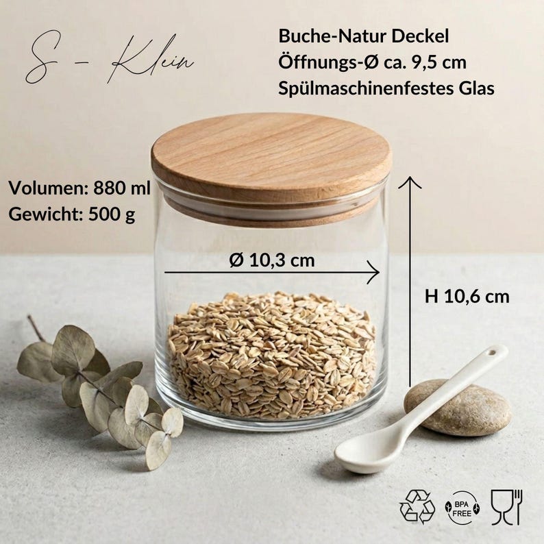 May include: A clear glass storage jar with a natural beech wood lid, filled with oats. Text indicates S-Klein, 880 ml volume, 500 g weight, 9.5 cm opening diameter, 10.3 cm diameter, and 10.6 cm height. Includes dishwasher-safe glass, BPA-free, and food-safe icons.