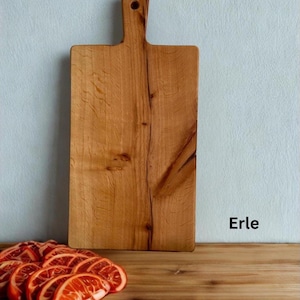 May include: A rectangular wooden cutting board with a handle and a hole for hanging, featuring a natural light brown wood grain pattern. The word Erle is printed in black text to the right of the board, near sliced orange fruit.