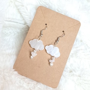 May include: A pair of white cloud-shaped earrings with silver hooks and white beads hanging from the bottom.