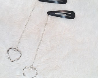 Puede incluir: Dos pinzas para el pelo negras con cadenas plateadas unidas a dijes de corazón de alambre de púas plateados.