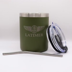 May include: Olive green tumbler with a silver rim and a clear lid. The tumbler has the name "LATIMER" and a winged emblem etched on the side. A silver metal straw is also included.