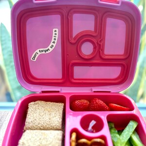 Pode incluir: Lancheira rosa com v&aacute;rios compartimentos. A lancheira est&aacute; aberta e cont&eacute;m um sandu&iacute;che, morangos, pretzels e aipo. Um adesivo na tampa diz "N&atilde;o se esque&ccedil;a de fazer uma bolus".
