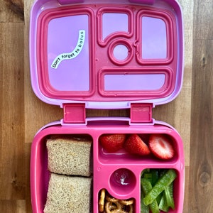 Pode incluir: Lancheira rosa com um adesivo que diz "Don't forget to bolus". A lancheira est&aacute; aberta e cont&eacute;m dois sandu&iacute;ches, morangos, piment&otilde;es verdes e pretzels.
