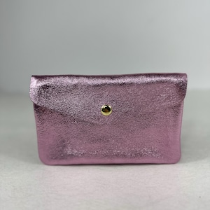 Könnte beinhalten: Eine kleine, rechteckige, metallisch rosa Clutch mit strukturierter Oberfläche. Die Clutch hat einen Klappenverschluss, der mit einem goldfarbenen Druckknopf gesichert ist. Das Accessoire wird wahrscheinlich zum Tragen kleiner Gegenstände verwendet.