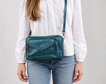 May include: A metallic teal crossbody bag with a rectangular shape, a front flap pocket, and a matching adjustable shoulder strap. The bag features a textured finish and is worn across the torso, showcasing a compact design with visible metal hardware.