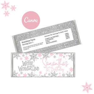 May include: Two decorative candy bar wrappers with a winter theme. The wrappers feature a silver glitter design and pink snowflakes. One wrapper says "Winter Wonderland" and "Samantha's 1st Birthday". The other wrapper has a nutrition facts label.