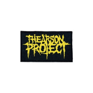May include: Black patch with the yellow text "The Arson Project" in a stylized font.