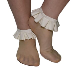Può includere: Polsini alla caviglia con volant bianco sporco. I polsini sono realizzati in un materiale morbido e presentano un design a pieghe. I polsini sono indossati attorno alle caviglie. Lo sfondo è bianco.