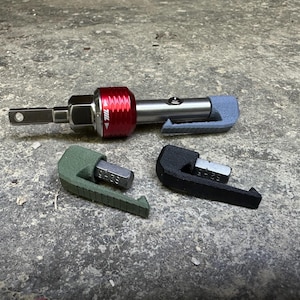 May include: A silver and red ratchet tool with a gray handle and three interchangeable bits. Two bits are green and black, and the tool is on a gray surface.