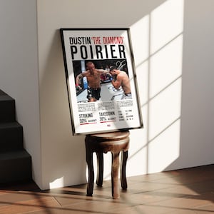 Peut inclure: Affiche encadrée de Dustin 'The Diamond' Poirier dans un cadre noir. L'affiche présente une photo de Poirier en action, avec des statistiques de frappe et de takedown. L'affiche est posée sur un petit tabouret en bois foncé.