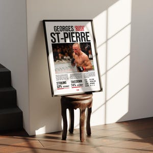 May include: A black and white poster with a photo of Georges St-Pierre, a mixed martial arts fighter, in a fighting stance. The poster has the text "GEORGES 'RUSH' ST-PIERRE" at the top and includes statistics about his striking and takedown accuracy.