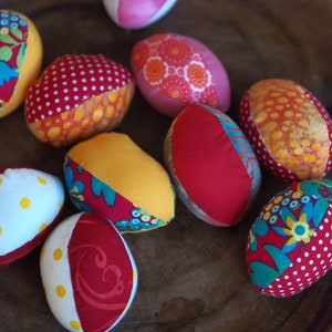 Könnte beinhalten: Neun bunte Stoff-Ostereier mit verschiedenen Mustern, darunter Punkte, Blumenmuster und geometrische Formen.