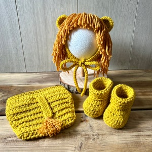 May include: A crocheted lion costume set for a baby, featuring a yellow hat with a mane, booties, and a matching nappy cover.