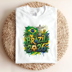 White t-shirt with "BRAZIL 2026" text, football, and Brazilian flag.