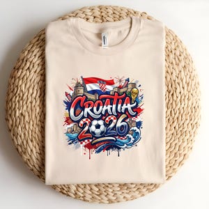 Cream t-shirt with "Croatia 2026" design featuring flags, fireworks, and waves.