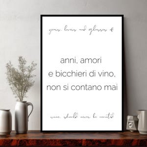 Pode incluir: Uma impressão emoldurada com texto preto sobre fundo branco. O texto inclui as frases "years, lovers and glasses of" e "wine should never be counted." A impressão é exibida em uma superfície de madeira escura com vasos decorativos e um pequeno jarro.