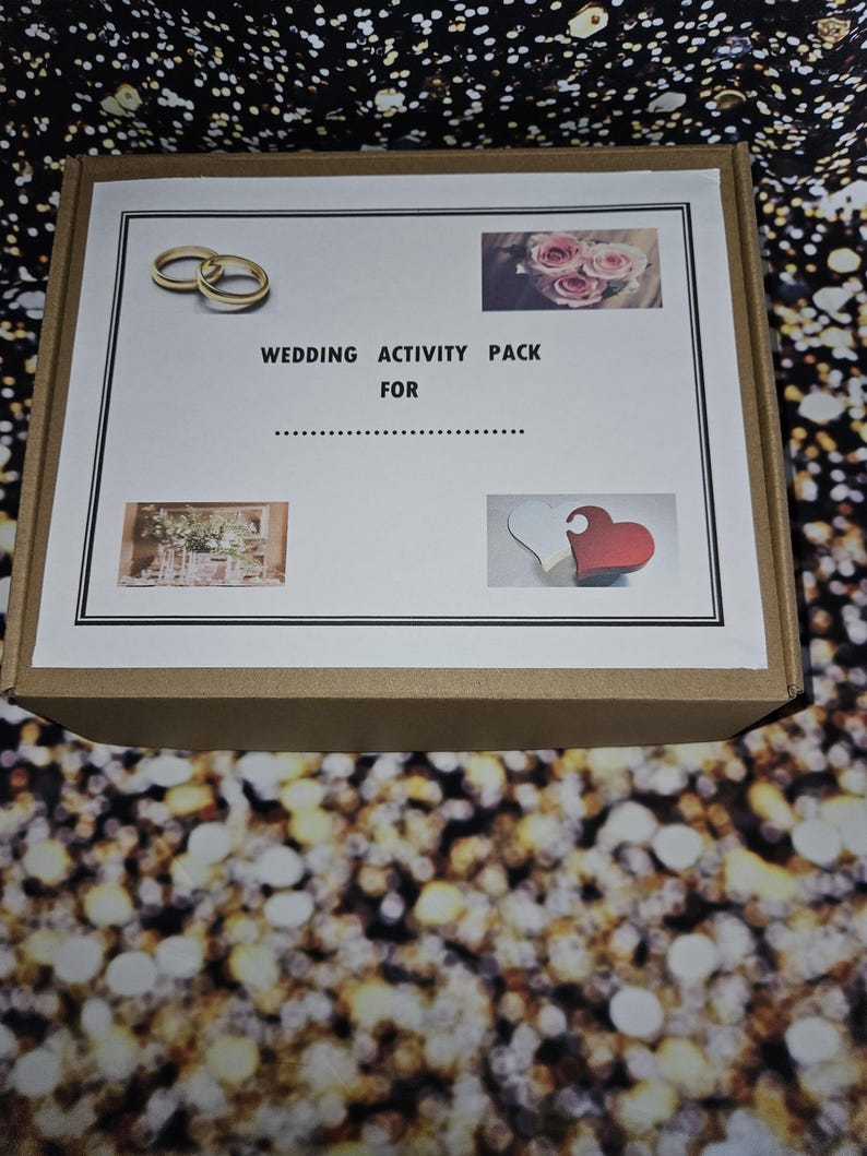 May include: A brown cardboard box with a white label that says "Wedding Activity Pack For". The label also has images of two gold rings, a bouquet of pink roses, and two wooden hearts.