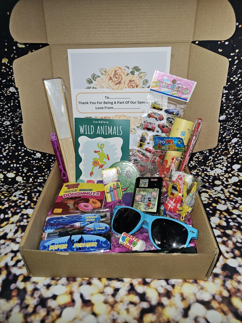 May include: A brown cardboard box filled with various items, including a book titled "Wild Animals", a pack of stickers, a pack of crayons, a pair of sunglasses, and a bag of gummy donuts. The box also includes a card with the text "Thank You For Being A Part Of Our Special Love From..."