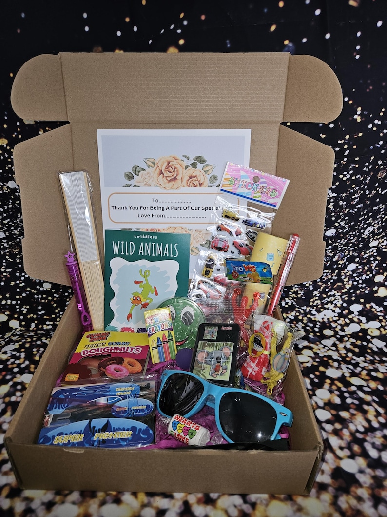 May include: A brown cardboard box filled with various items, including a coloring book titled "Wild Animals", crayons, stickers, sunglasses, a fan, and a bag of donuts. The box also includes a card with the text "To... Thank You For Being A Part Of Our Special... Love From..."