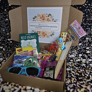 May include: A brown cardboard box filled with party favors, including a book titled "Wild Animals", candy, stickers, and sunglasses. The box has a card on top that says "Thank You For Being A Part Of Our Special Day".