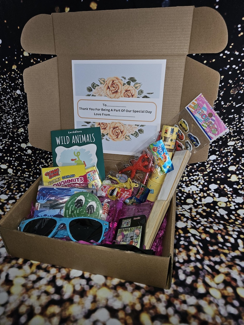 May include: A brown cardboard box filled with party favors, including a book titled "Wild Animals", candy, stickers, and sunglasses. The box has a card on top that says "Thank You For Being A Part Of Our Special Day".