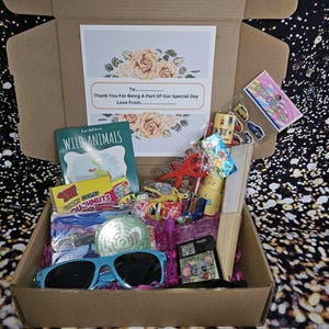 May include: A brown cardboard box filled with various party favors, including a book about wild animals, a pack of stickers, a pack of gummy candies, a pair of blue sunglasses, and a small wooden fan. The box also includes a card with the text "To... Thank You For Being A Part Of Our Special Day Love From..."