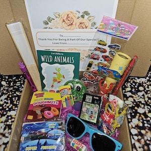 May include: A gift box filled with various items, including a coloring book, crayons, stickers, a fan, sunglasses, and candy. The box is lined with pink tissue paper. The box has a card with the text "Thank You For Being A Part Of Our Special Day Love From..."