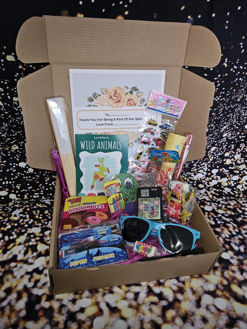 May include: A brown cardboard box filled with various items, including a book titled "Wild Animals", a bag of gummy doughnuts, a pair of blue sunglasses, and a variety of colorful toys and trinkets. The box is open and the items are visible inside.