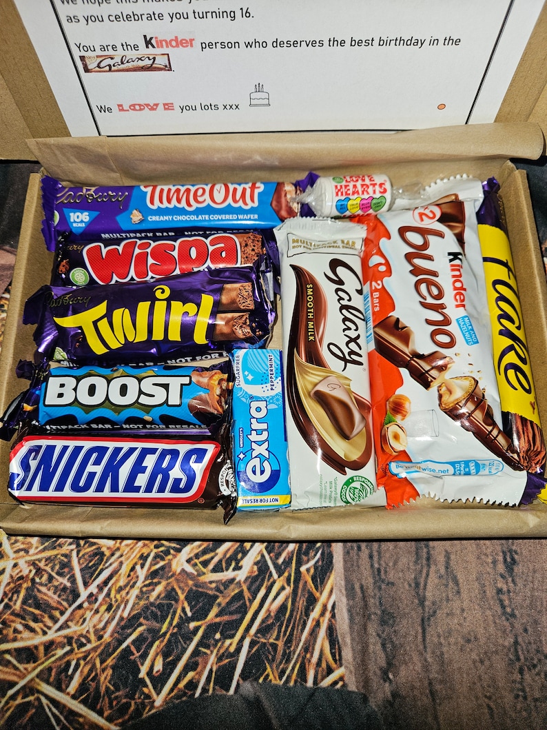 May include: A box filled with various chocolate bars, including Twirl, Wispa, Galaxy, Kinder Bueno, and Snickers. The box also contains a small bag of Love Hearts candy.