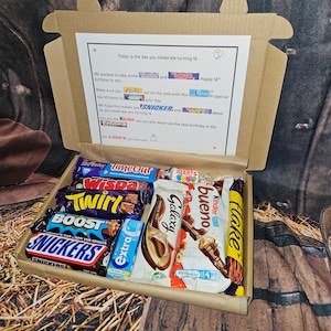 May include: A brown cardboard box filled with a variety of chocolate bars. The box has a note inside that says "Today is the day you celebrate turning 16." The note also includes the names of the chocolate bars: "Time Out", "Wispa", "Twirl", "Boost", "Snickers", "Galaxy", "Bueno", "Kinder", "Flake", and "Extra".