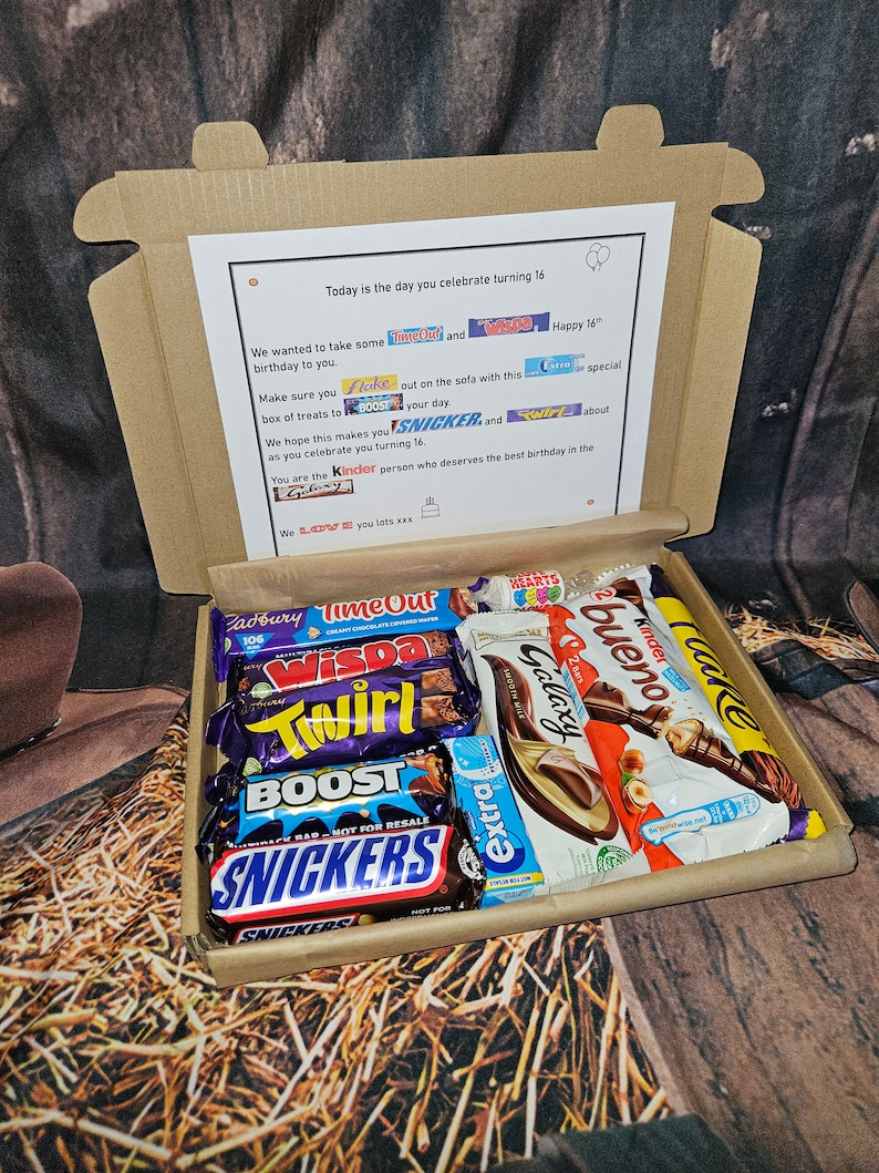 May include: A brown cardboard box filled with a variety of chocolate bars, including Twirl, Wispa, Galaxy, Kinder Bueno, and Snickers. The box is decorated with a birthday message and a list of chocolate brands.