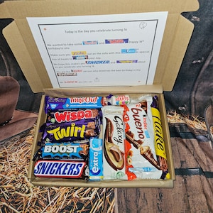 May include: A brown cardboard box filled with a variety of chocolate bars, including Snickers, Twirl, Galaxy, Wispa, Time Out, Kinder Bueno, Boost, and Flake. The box is decorated with a card that says "Today is the day you celebrate turning 16. Happy 16th."