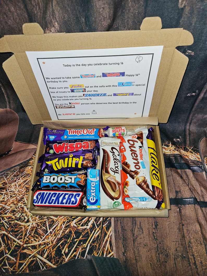 May include: A brown cardboard box filled with a variety of chocolate bars, including Snickers, Twirl, Galaxy, Wispa, Time Out, Kinder Bueno, Boost, and Flake. The box is decorated with a card that says "Today is the day you celebrate turning 16. Happy 16th."