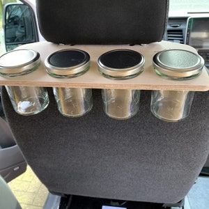 May include: A wooden shelf with four glass jars with metal lids attached to the back of a car seat.