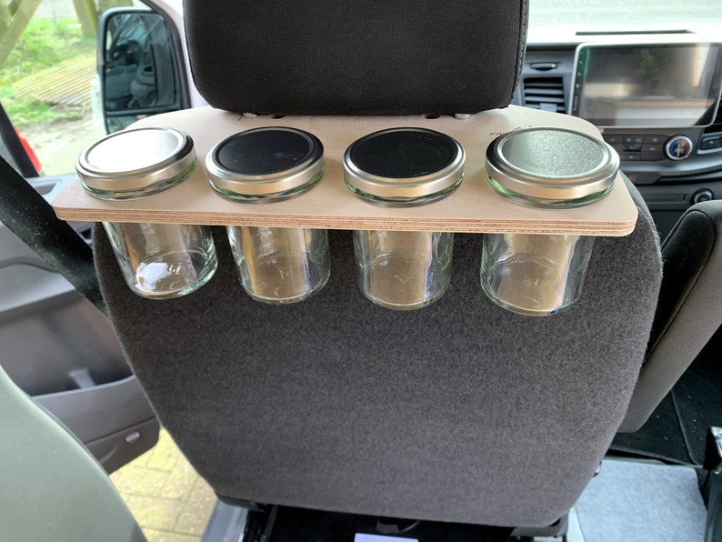 May include: A wooden shelf with four glass jars with metal lids attached to the back of a car seat.