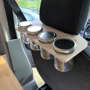 May include: A wooden shelf with four glass jars with silver lids attached to the headrest of a car seat. The shelf is labeled "Camp Kitchen".