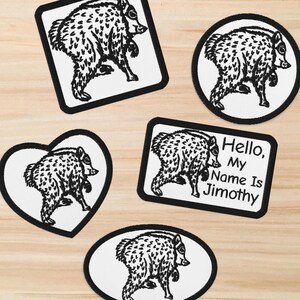 May include: Five embroidered patches featuring a black and white illustration of a javelina. The patches are square, circular, heart-shaped, rectangular with the text "Hello, My Name Is Jimothy," and oval. Each patch has a thick black border.